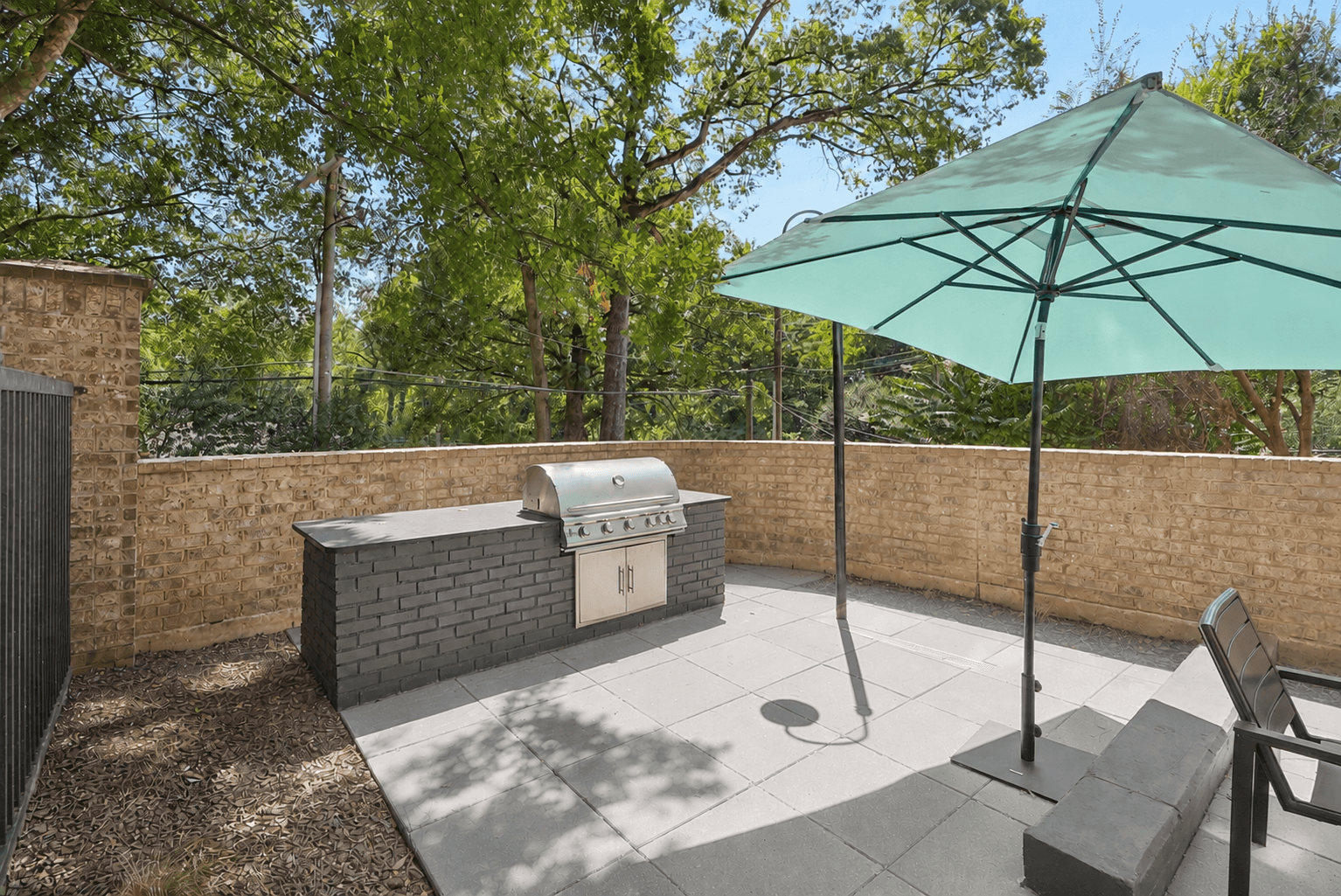 A patio with a green umbrella and a brick wall.